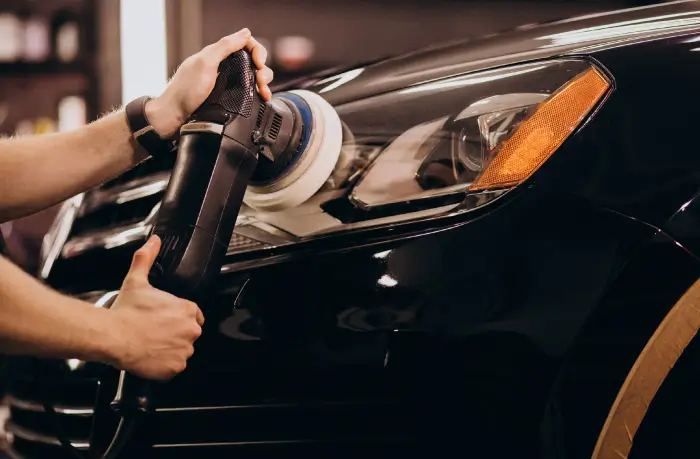 Close-up of a professional car detailing process with a buffer polishing the headlight area on a black car