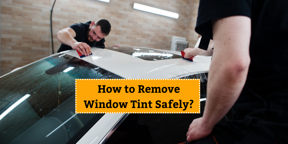 Two workers carefully removing window tint from a car's windshield using tools, demonstrating the safe process of tint removal.