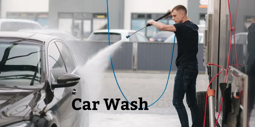 Person washing a black car at a car wash station with a high-pressure water hose