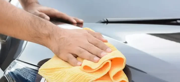 A person buffing and cleaning a car’s hood with a soft cloth, creating a polished, shiny surface.