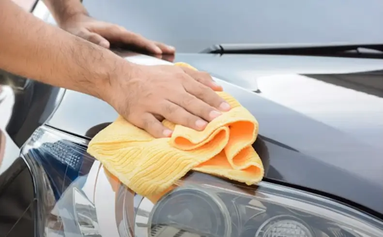 A person buffing a car’s hood with a soft cloth, creating a polished, shiny surface.