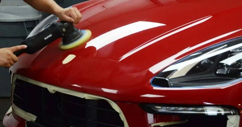 Car hood being buffed to a high gloss finish with a professional polishing tool.