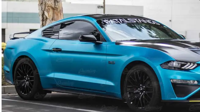 A vibrant blue Ford Mustang with a black hood, tinted windows, and custom decals parked near trees