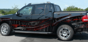 A black pickup truck with custom red and black carbon fiber-style graphic vinyl wrap and chrome wheels