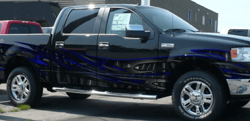 A sleek black pickup truck with vibrant blue flame decals and chrome wheels, parked outdoors near a dealership.