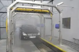 A black car passing through an automated car wash tunnel with mist and cleaning equipment surrounding it