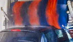 Car going through an automatic car wash with large rotating brushes in red and blue applying soap and water