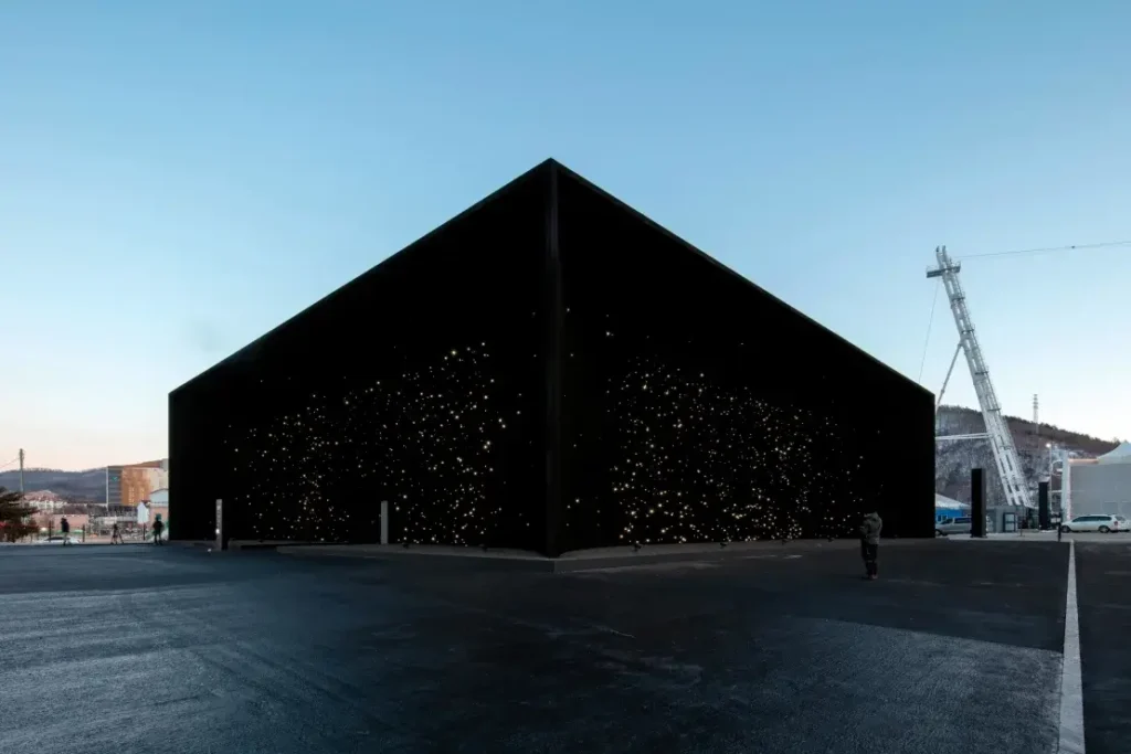 A black cube-shaped building coated in Vantablack, appearing as if it absorbs all light, with faint star-like dots visible.