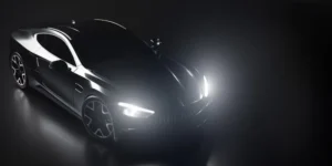 Luxurious black sports car with bright headlights illuminating a dark studio