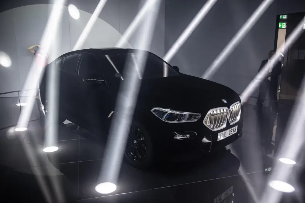 A BMW X6 coated in Vantablack, displayed under dramatic lighting with beams of light highlighting its unique ultra-black finish