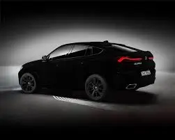 A stylish black luxury BMW with a bold front grille and sleek design, illuminated under a soft spotlight in a minimalist setting