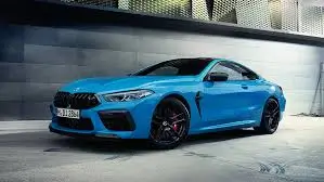 A vibrant blue BMW M8 coupe parked near a modern building, emphasizing its sporty and luxurious design.