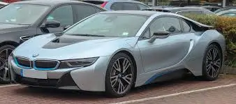 A sleek silver BMW i8 parked in a parking lot, showcasing its futuristic hybrid sports car design.