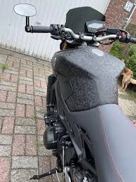 A close-up side view of a sleek motorcycle with a subtle patterned design on the tank and a minimalist black-gray finish.