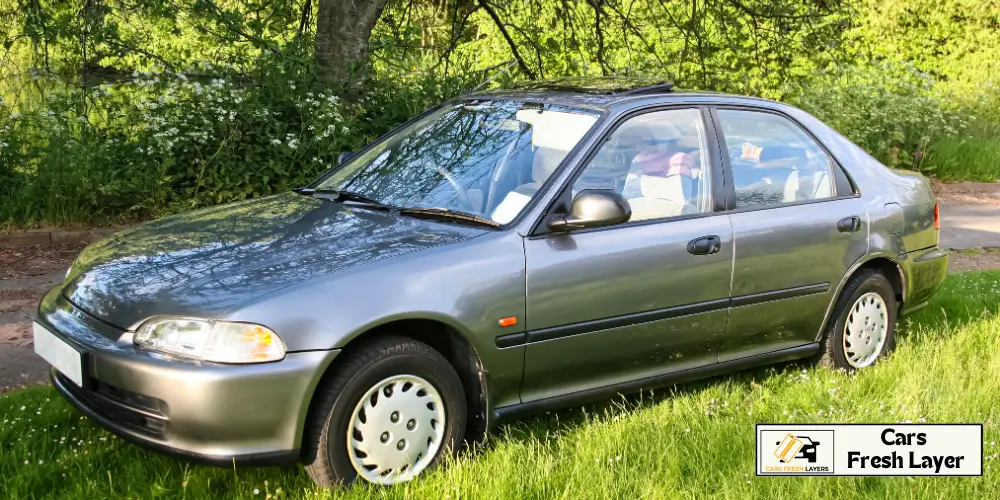 Compact silver sedan parked by lush greenery on a sunny day.Honda Civic (likely EG generation