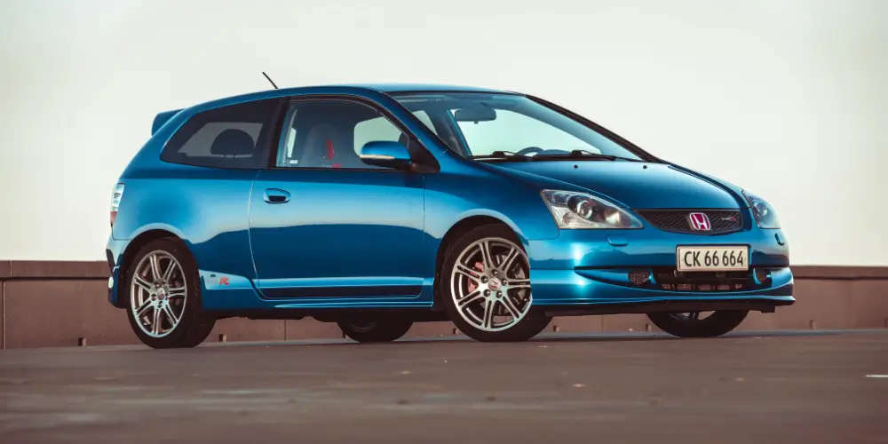 A vibrant blue Honda Civic R with sporty alloy wheels, parked under a clear sky, showcasing its sleek and stylish design.